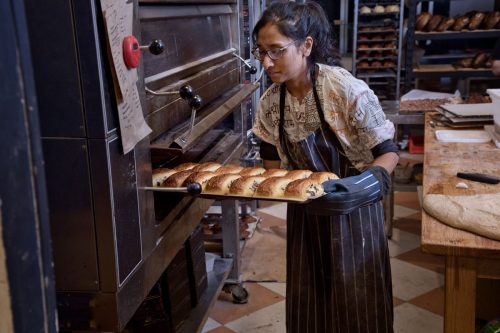 Behind the scenes of Flour Shop bakery as a baker pulls baked goods out of an oven