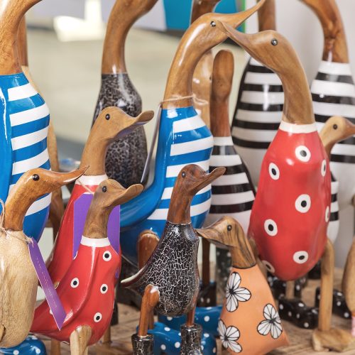14 glossy wooden ducks with various painted outfits on timber counter